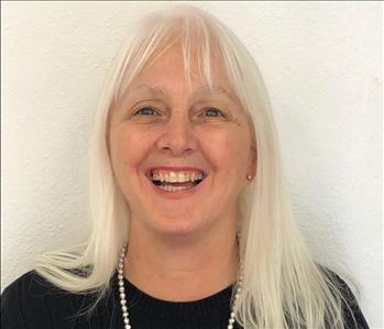 Smiling female employee with white hair, pearl necklace and black shirt.