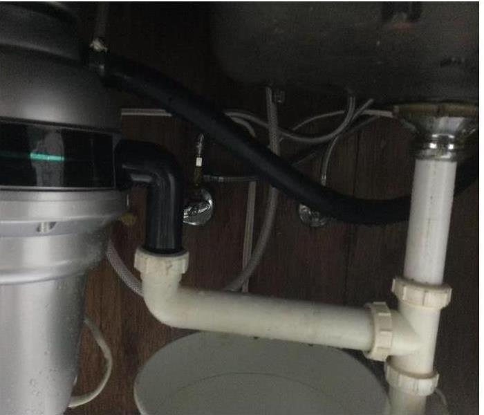 Grey garbage disposal, black and white pipes under sink.